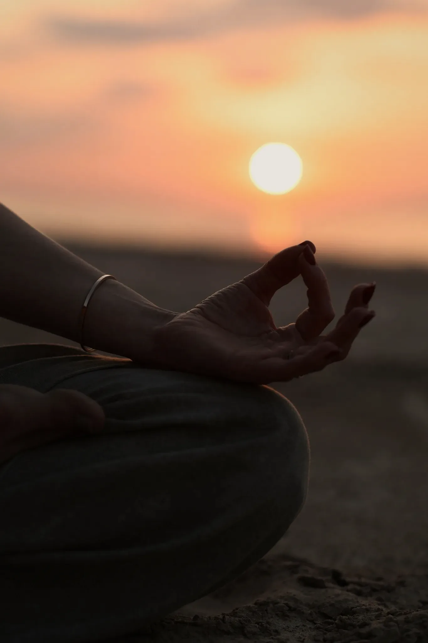 A hand resting in a meditation mudra against a sunrise.