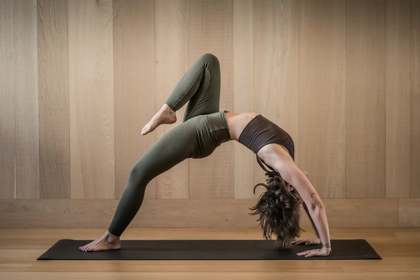 A deep backbend held on a mat in a wood-panelled room.