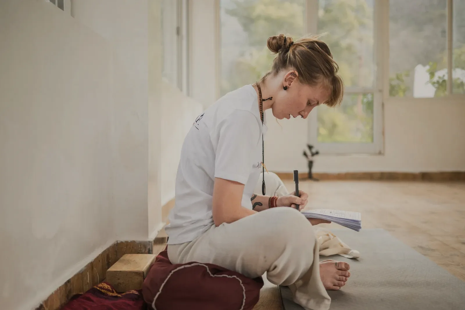 A person writing in a notebook by a window in the morning.