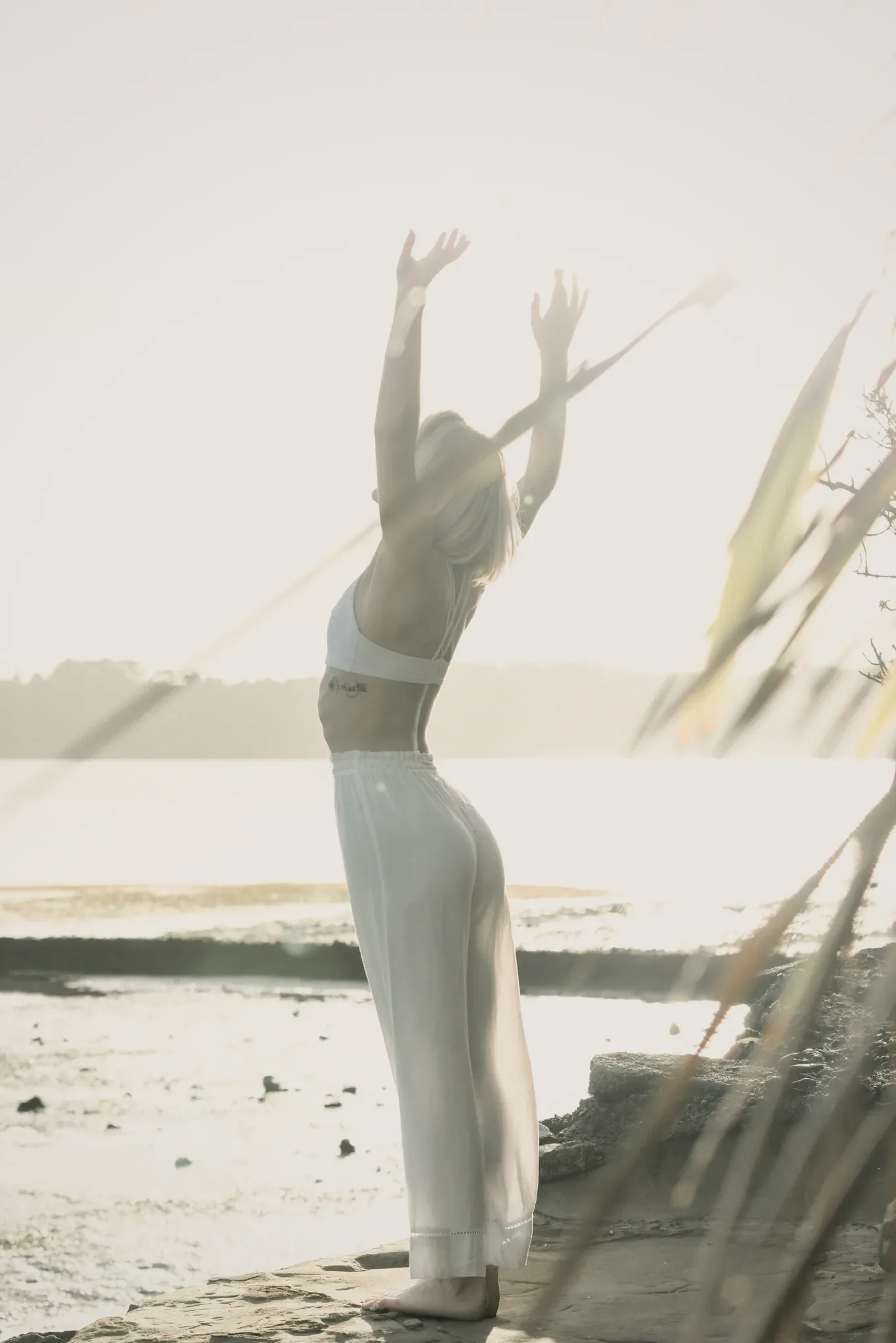 A person stretching upward in bright sunlight by the sea.