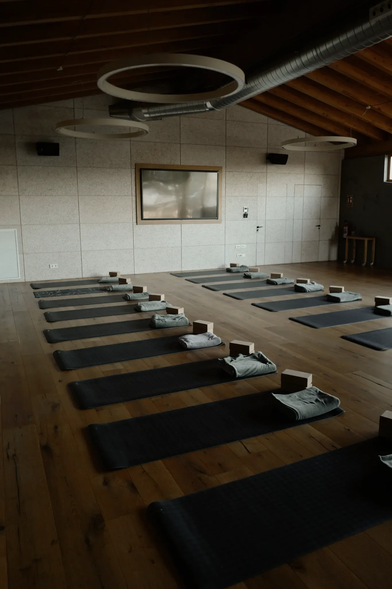 A studio with rows of mats, blocks and folded towels on a wooden floor.