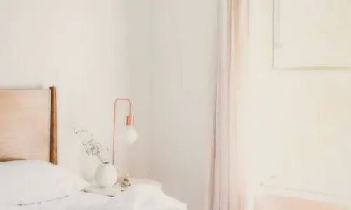 A white bedroom with a copper lamp and linen curtains.