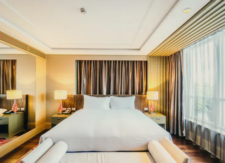 A hotel bedroom with a wide bed and brown curtains.