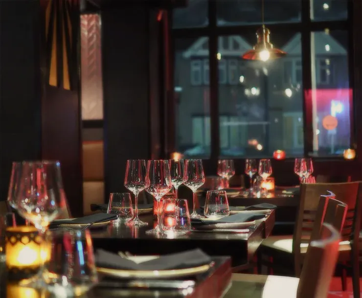 A dim restaurant with set tables and pendant lights.