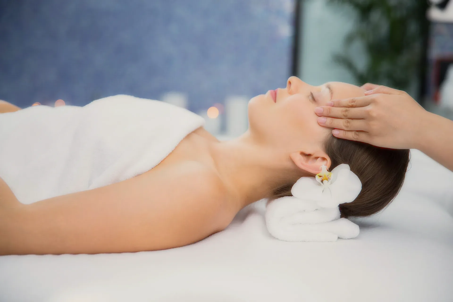 A woman resting during a face massage, a white flower by her ear.