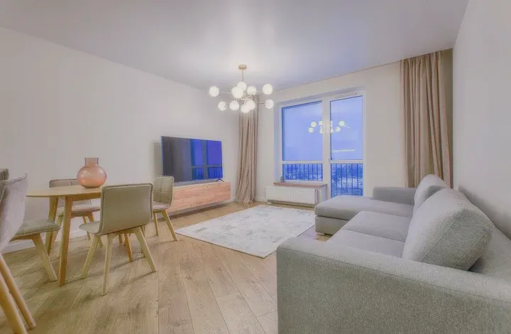 A bright living area with a grey sofa, a round dining table and a chandelier.