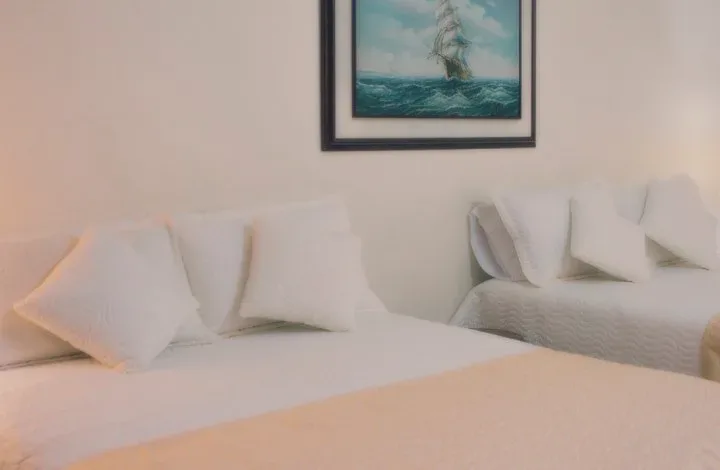 A white bed with many pillows under a painting of a ship at sea.