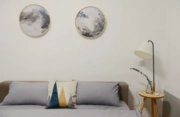 A white room with a grey sofa, two round prints and a floor lamp.