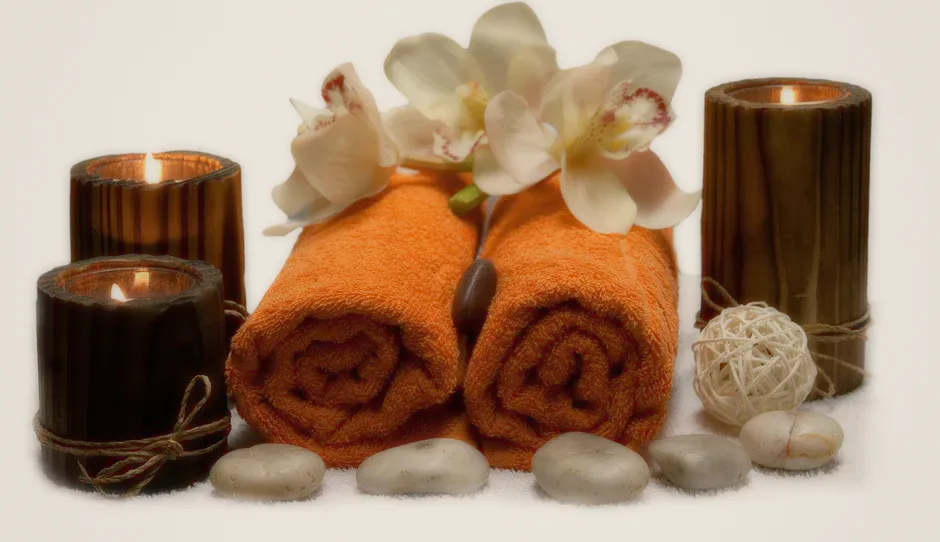 Rolled orange towels, candles, stones and white orchids.