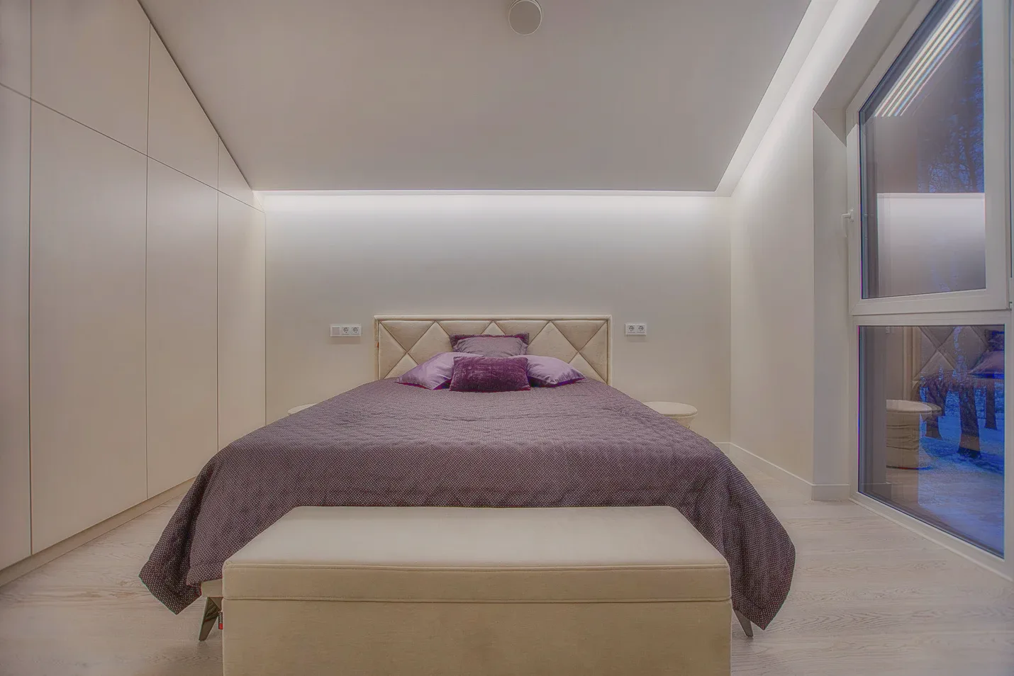 A bedroom with a quilted headboard, a purple bedspread and a bench at its foot.